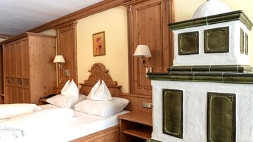 Ein gemütliches Schlafzimmer mit Holzverkleidung und zwei Betten. Eine traditionelle Kachelheizung fügt dem Raum einen rustikalen Charme hinzu.