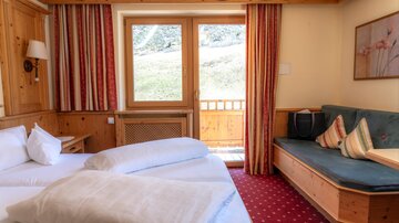 Ein gemütliches Hotelzimmer mit einem Doppelbett und einer Sitzecke. Durch die Fenster ist eine grüne Landschaft zu sehen.