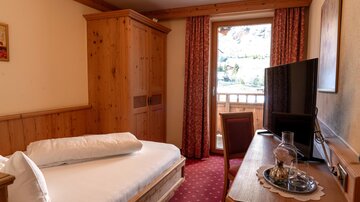Ein gemütliches Zimmer mit Holzverkleidung und einem Einzelbett. Es gibt einen Fernseher, einen Tisch und einen Balkon mit Blick nach draußen.
