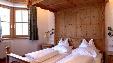 Ein gemütliches Schlafzimmer mit einem Holzbett und zwei bequemen Kissen. Die Fenster bieten viel Licht und der Raum ist im rustikalen Stil eingerichtet.
