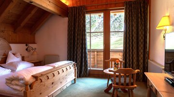 Ein gemütliches Schlafzimmer mit Holzdetails und zwei Fenstern. Es gibt ein Bett, einen Tisch mit Stühlen und viel Tageslicht.