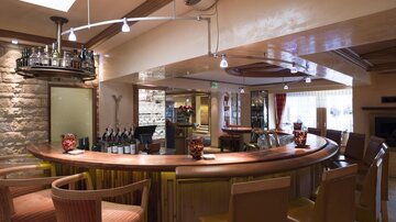 Eine elegante Bar mit Holztheke und stilvollen Stühlen. Im Hintergrund sind Flaschen und Gläser ordentlich aufgereiht.