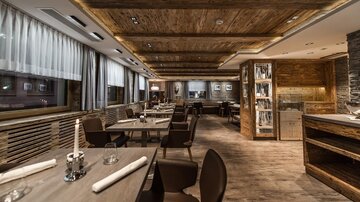 Ein elegantes Restaurant mit Holzmöbeln und warmem Licht. Die Tische sind für Gäste gedeckt und schaffen eine gemütliche Atmosphäre.