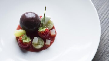Ein elegantes Dessert auf einem weißen Teller. Es besteht aus einer runden Schokoladensorte und verschiedenen frischen Früchten.