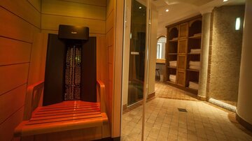 Ein gemütlicher Wellnessbereich mit einer Infrarotbank und großen Regalen voller Handtücher. Sanfte Beleuchtung und warme Farben schaffen eine entspannende Atmosphäre.