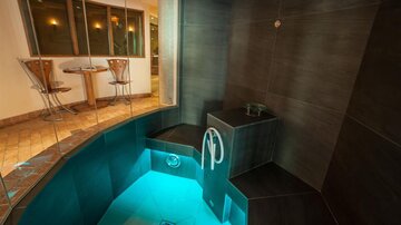 Ein modernes Dampfbad mit sanft beleuchtetem Wasser und stilvollen Kacheln. Im Hintergrund sind Tisch und Stühle zu sehen.