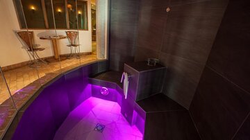 Ein luxuriöser Wellnessbereich mit einem runden, sanft beleuchteten Pool. Die Wände sind dunkel, und es gibt moderne Sitzgelegenheiten im Hintergrund.